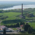Scenic rural area with a historic factory, lush greenery, and flowing river.