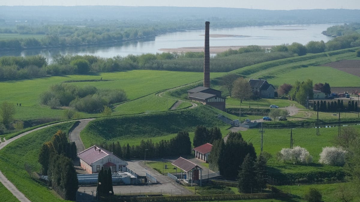 Scenic rural area with a historic factory, lush greenery, and flowing river.